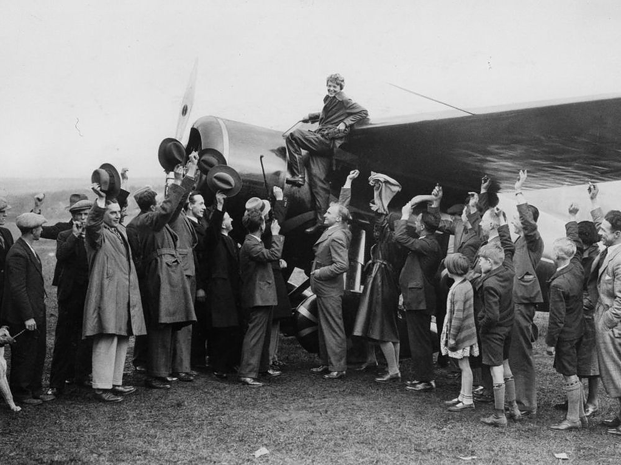 Earhart stands near airplane wing as people cheer
